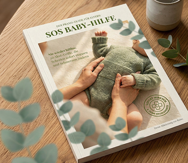 Gedruckter SOS Baby-Hilfe Guide auf einem Holztisch mit Eukalyptuszweigen, Praxis-Guide mit Akupressur-Griffen für Babys von 0 bis 18 Monaten
